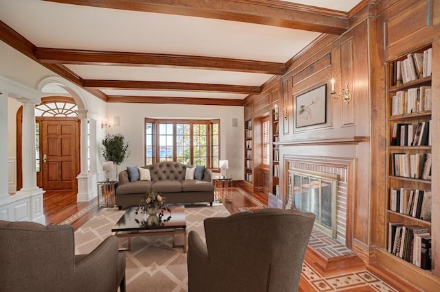 living room with decorative columns, light hardwood / wood-style flooring, beamed ceiling, and a brick fireplace