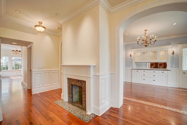 unfurnished living room featuring a fireplace, wood-type flooring, a chandelier, and crown molding