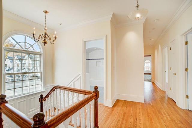 hallway featuring light wood-type flooring, ornamental molding, and a chandelier