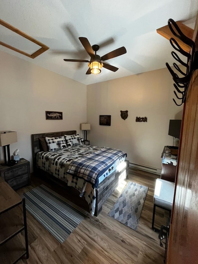 bedroom featuring ceiling fan, a baseboard heating unit, and wood-type flooring