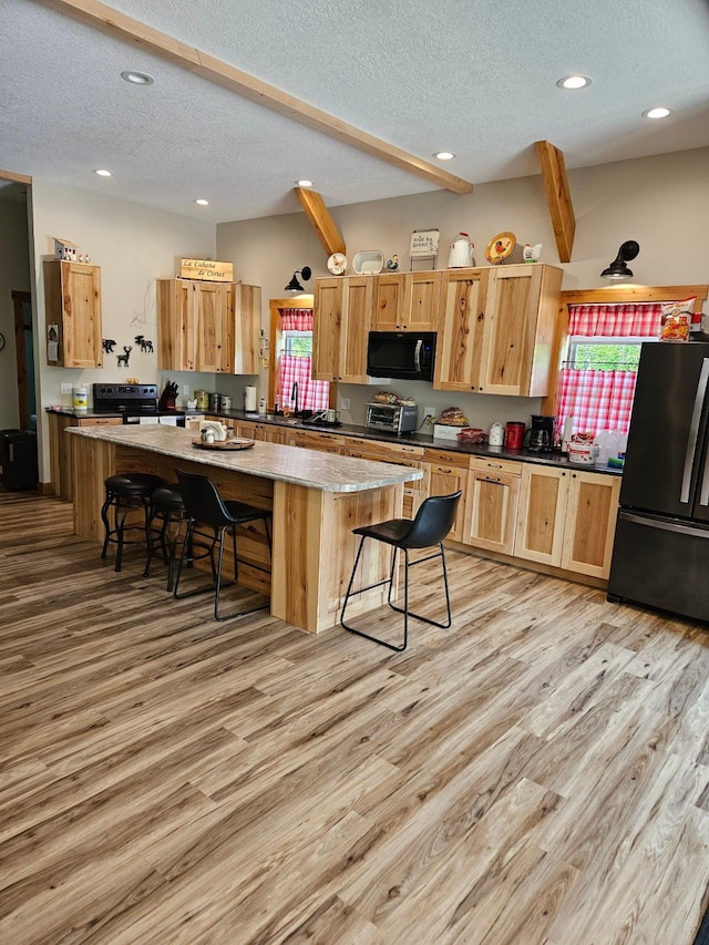 kitchen with a breakfast bar, black appliances, light hardwood / wood-style floors, and a center island