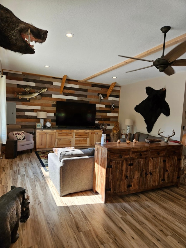 living room with wood-type flooring, a textured ceiling, wooden walls, and ceiling fan