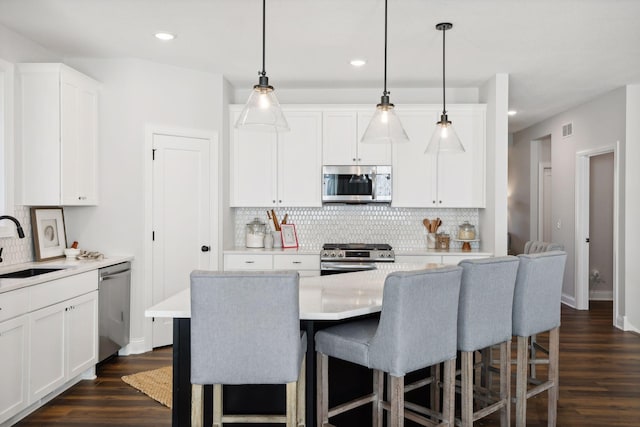 kitchen with stainless steel appliances, sink, decorative light fixtures, white cabinets, and a kitchen island