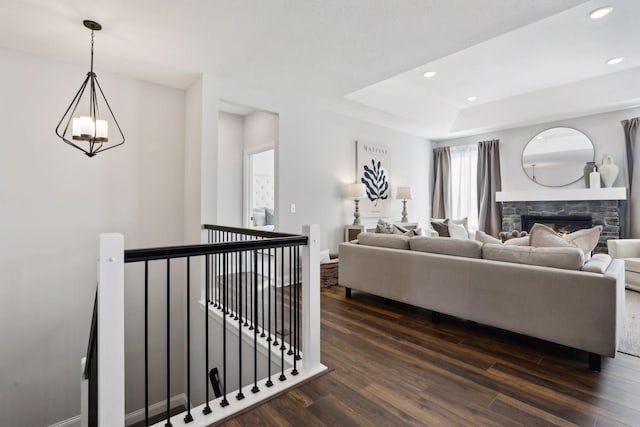 living room featuring a raised ceiling, a stone fireplace, dark wood-type flooring, and an inviting chandelier