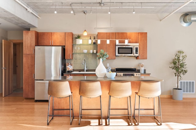 kitchen with light wood-type flooring, appliances with stainless steel finishes, a kitchen bar, and sink