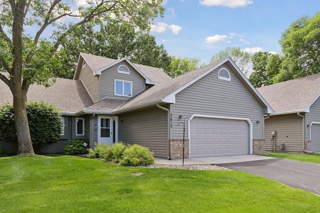 view of front facade featuring aphalt driveway, a garage, a shingled roof, brick siding, and a front lawn