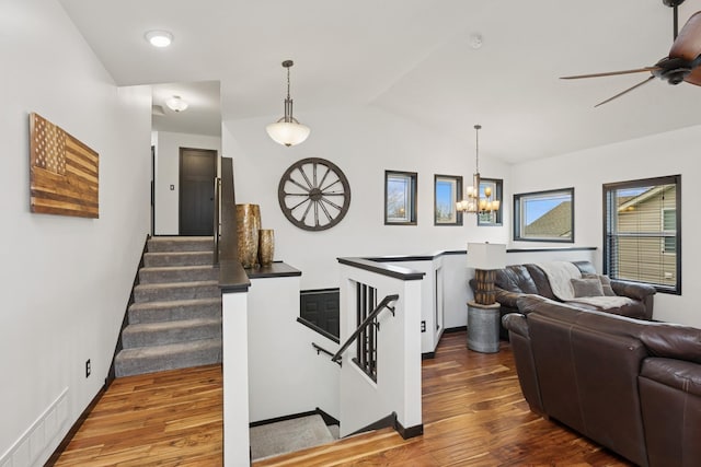 living area featuring visible vents, wood finished floors, baseboards, ceiling fan with notable chandelier, and lofted ceiling