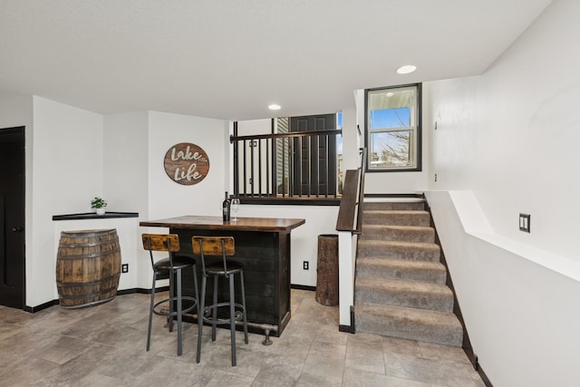bar featuring recessed lighting, wet bar, baseboards, and stairway