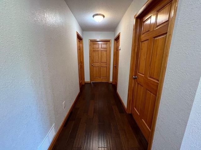 hallway with a textured ceiling and dark hardwood / wood-style floors