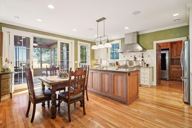 kitchen featuring stainless steel refrigerator, fridge, range hood, light hardwood / wood-style floors, and decorative light fixtures