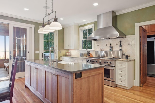 kitchen with stainless steel stove, backsplash, extractor fan, a center island with sink, and decorative light fixtures