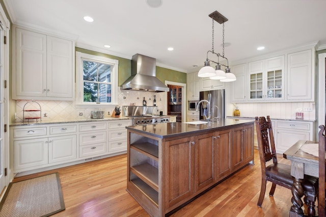 kitchen with extractor fan, hanging light fixtures, light wood-type flooring, an island with sink, and white cabinets