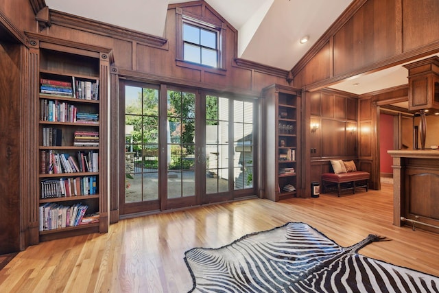 sitting room with built in features, wooden walls, vaulted ceiling, and light hardwood / wood-style flooring