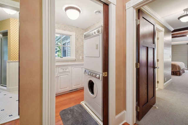 washroom featuring crown molding, stacked washer / drying machine, and light hardwood / wood-style floors