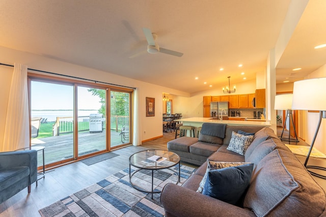 living room with ceiling fan with notable chandelier, light wood-type flooring, a water view, and vaulted ceiling