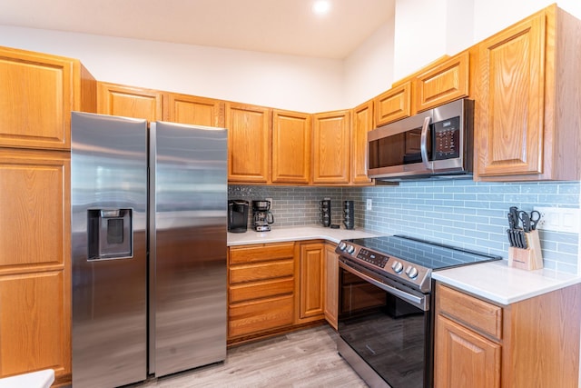 kitchen featuring backsplash, appliances with stainless steel finishes, light wood-type flooring, and vaulted ceiling