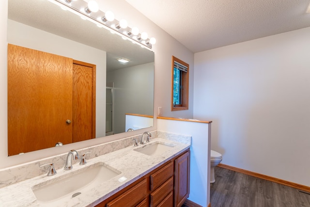 bathroom with wood-type flooring, vanity, toilet, and a textured ceiling