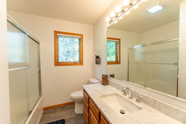 full bathroom with a textured ceiling, hardwood / wood-style floors, bath / shower combo with glass door, vanity, and toilet