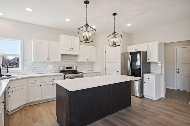 kitchen with white cabinets, appliances with stainless steel finishes, light hardwood / wood-style flooring, sink, and a center island