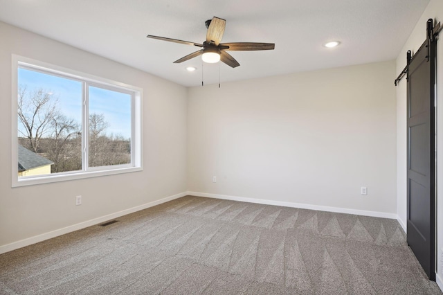 unfurnished bedroom featuring a barn door, carpet flooring, and ceiling fan