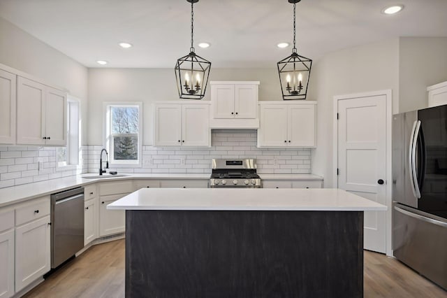 kitchen with stainless steel appliances, sink, a center island, pendant lighting, and white cabinetry