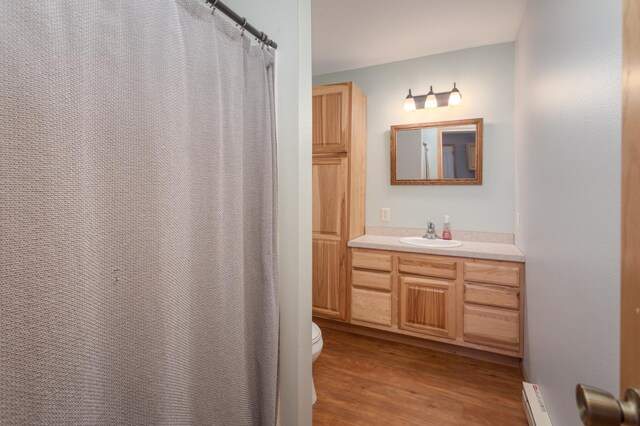 11421 Abby Ln NW, Alexandria, MN 56308 - full bathroom with vanity, wood finished floors, toilet, a baseboard heating unit, and a shower with curtain