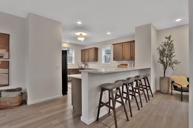 kitchen featuring kitchen peninsula, a kitchen breakfast bar, light hardwood / wood-style floors, and black fridge