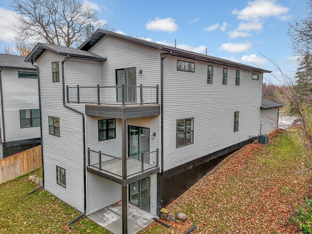 rear view of property with a balcony, cooling unit, and a lawn