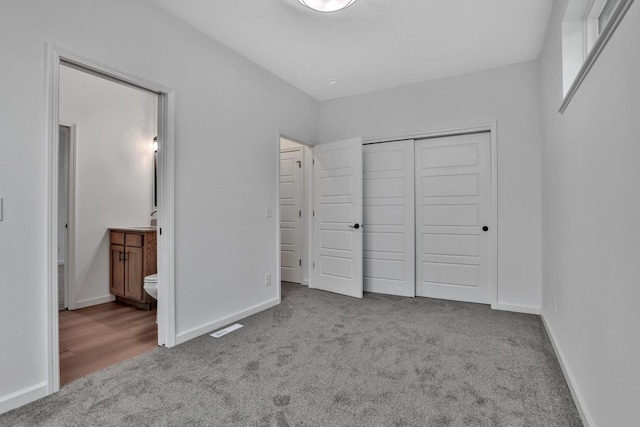 unfurnished bedroom with light colored carpet, a closet, and ensuite bathroom