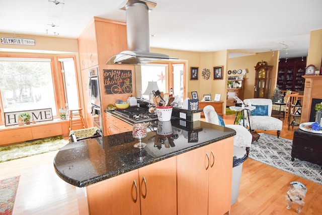 kitchen featuring dark stone counters, island range hood, double oven, stainless steel gas cooktop, and light hardwood / wood-style floors