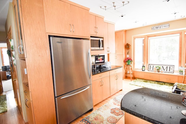 kitchen featuring appliances with stainless steel finishes, light brown cabinetry, light hardwood / wood-style floors, and dark stone counters