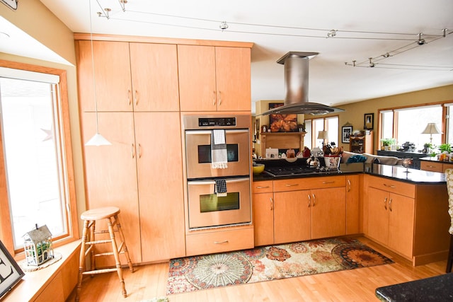 kitchen with island exhaust hood, kitchen peninsula, light wood-type flooring, stainless steel double oven, and gas stovetop