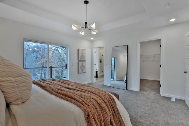 carpeted bedroom featuring access to outside, a tray ceiling, a spacious closet, a notable chandelier, and a closet