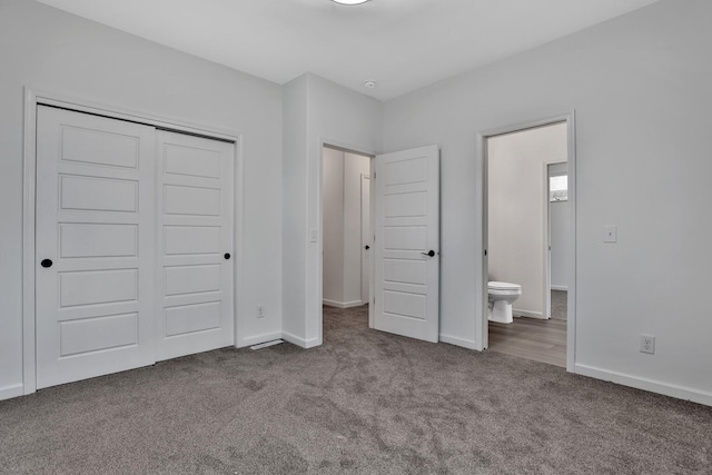 unfurnished bedroom with ensuite bathroom, dark carpet, and a closet