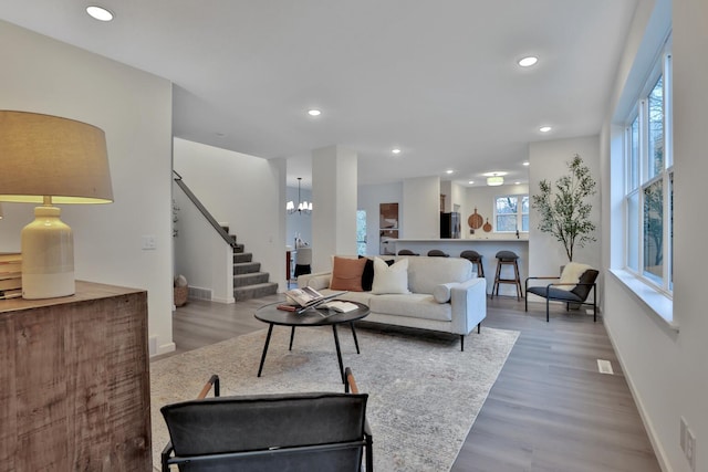 living area featuring recessed lighting, stairway, an inviting chandelier, wood finished floors, and baseboards