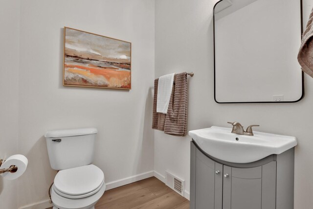 half bath featuring toilet, baseboards, visible vents, wood finished floors, and vanity