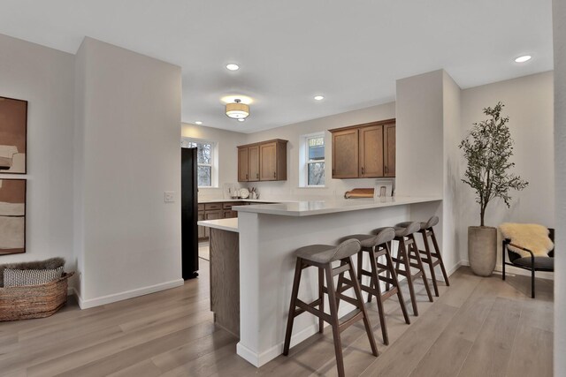 kitchen with light wood finished floors, freestanding refrigerator, recessed lighting, and a kitchen bar