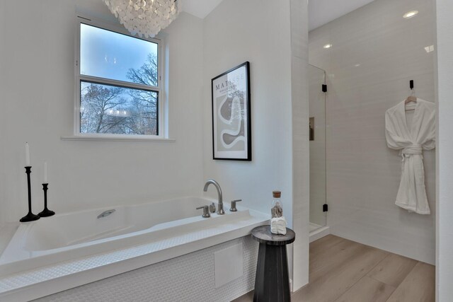 full bath featuring a bath, wood finished floors, a chandelier, and a stall shower