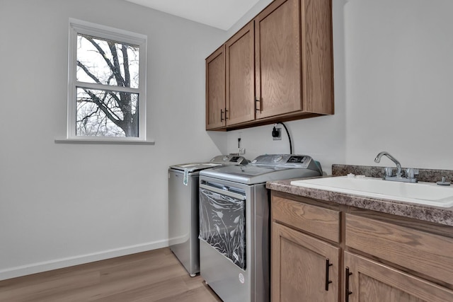 laundry area featuring washing machine and clothes dryer, light wood finished floors, a sink, baseboards, and cabinet space