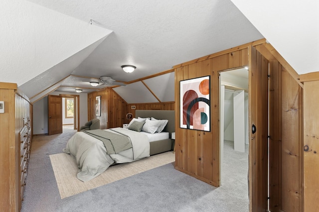 bedroom with a walk in closet, vaulted ceiling, light colored carpet, a textured ceiling, and wood walls