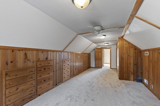 bonus room with wood walls, vaulted ceiling, light colored carpet, a textured ceiling, and ceiling fan