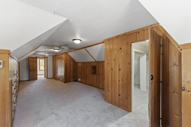 bonus room featuring ceiling fan, a textured ceiling, lofted ceiling, and wooden walls