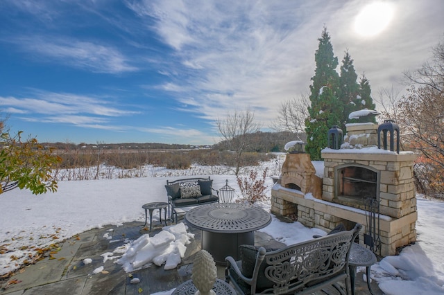 snow covered patio with an outdoor stone fireplace