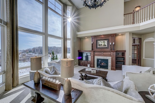 carpeted living room featuring a stone fireplace, an inviting chandelier, and a high ceiling