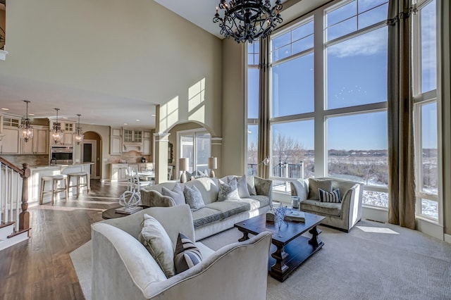 living room with a wealth of natural light, a chandelier, light hardwood / wood-style flooring, and a towering ceiling