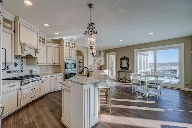 kitchen featuring dark wood-type flooring, an island with sink, sink, pendant lighting, and appliances with stainless steel finishes