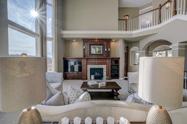 carpeted living room featuring decorative columns, a stone fireplace, and a towering ceiling