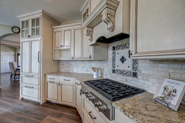 kitchen with tasteful backsplash, dark hardwood / wood-style floors, cream cabinetry, stainless steel gas cooktop, and light stone counters