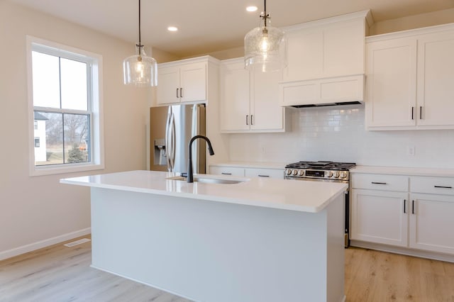 kitchen with white cabinets, sink, hanging light fixtures, an island with sink, and stainless steel appliances