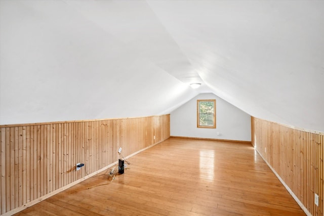 bonus room with light hardwood / wood-style flooring, lofted ceiling, and wood walls